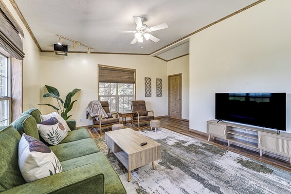 A living room with a green sofa, a coffee table, a TV, and a ceiling fan. - History & Nature Hub! Family Gem in Fayetteville (Fayetteville)