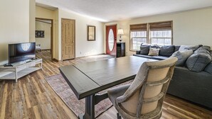 Un salon comprenant une grande table en bois foncé, un canapé, un téléviseur et une porte dotée d’un panneau en verre rouge.