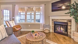 A living room with a fireplace, a sofa, a coffee table, and a large window with curtains. - Modern Black Mountain Cottage: 17 Mi to Asheville! (Black Mountain)