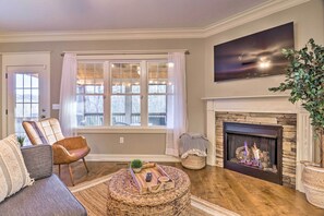 Ein Wohnzimmer mit Kamin, einer Couch, einem Couchtisch und einem großen Fenster mit Vorhängen.