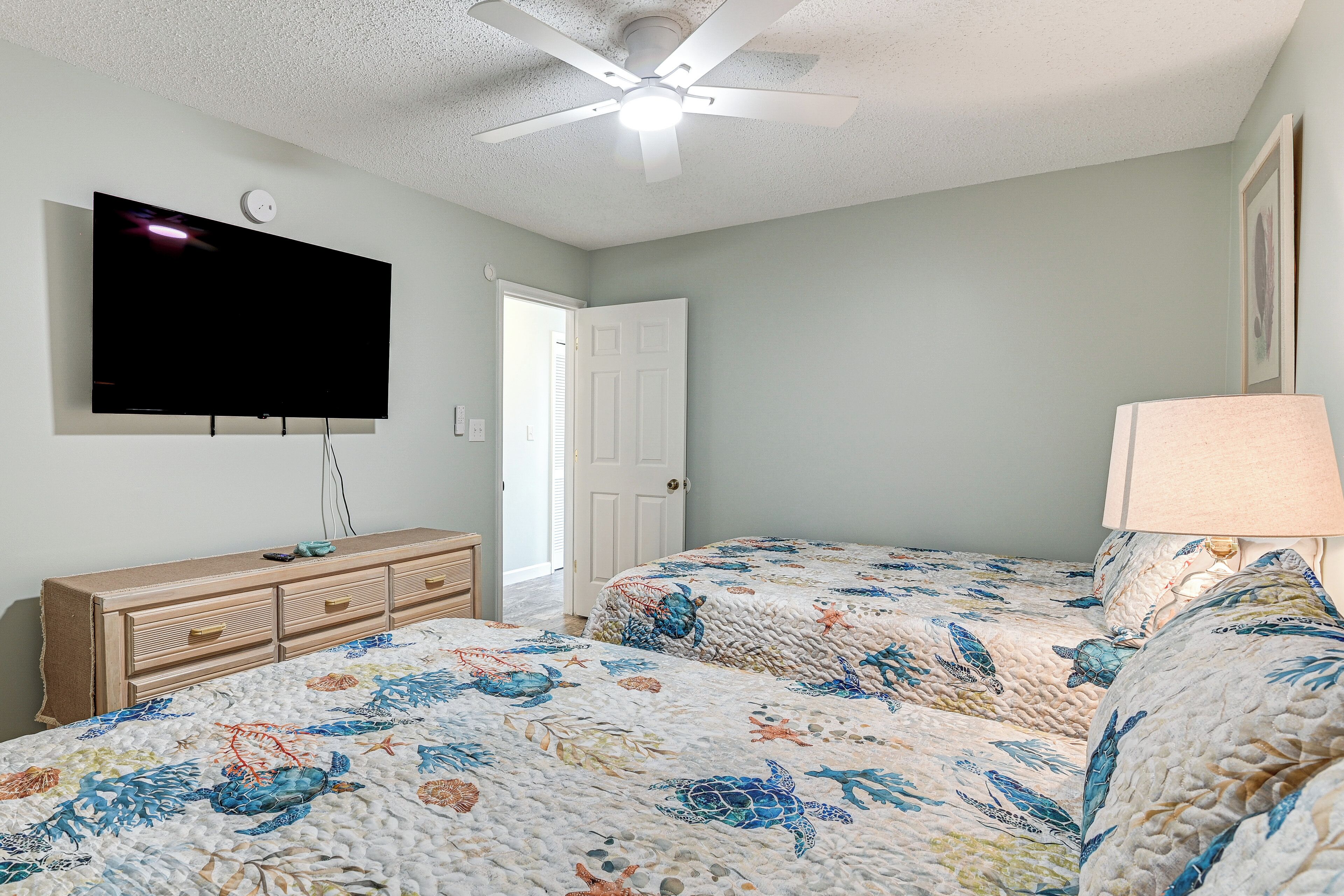 A bedroom with a bed, a dresser, a television, and a ceiling fan.