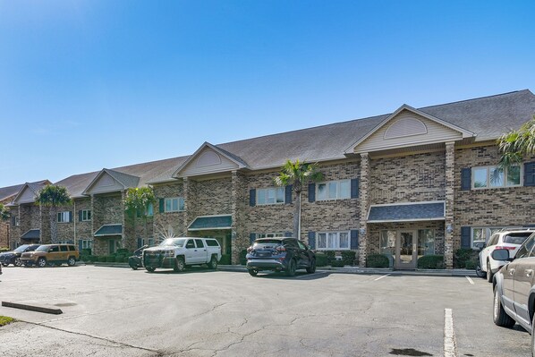 A multi-story building with a brick facade, multiple parking spaces, and a clear blue sky. - Water-view Patio! Condo 2 Mi to Surfside Beach (Surfside Beach)