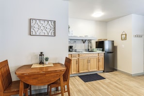 A modern kitchen with wooden cabinets, a stainless steel refrigerator, and a dining area with a wooden table and chairs.