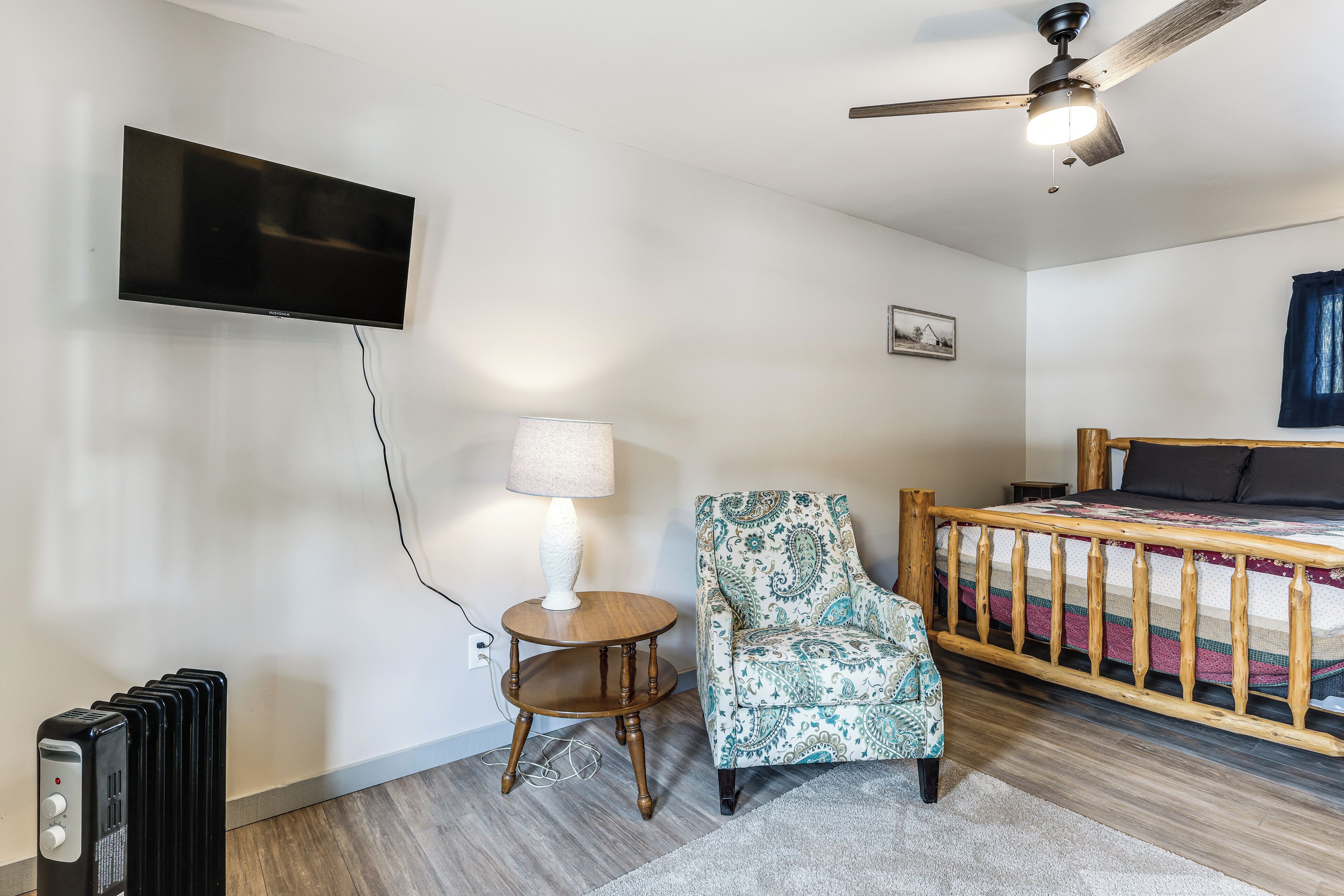 Un dormitorio con cama, televisión, calefactor, sillón y ventilador de techo.