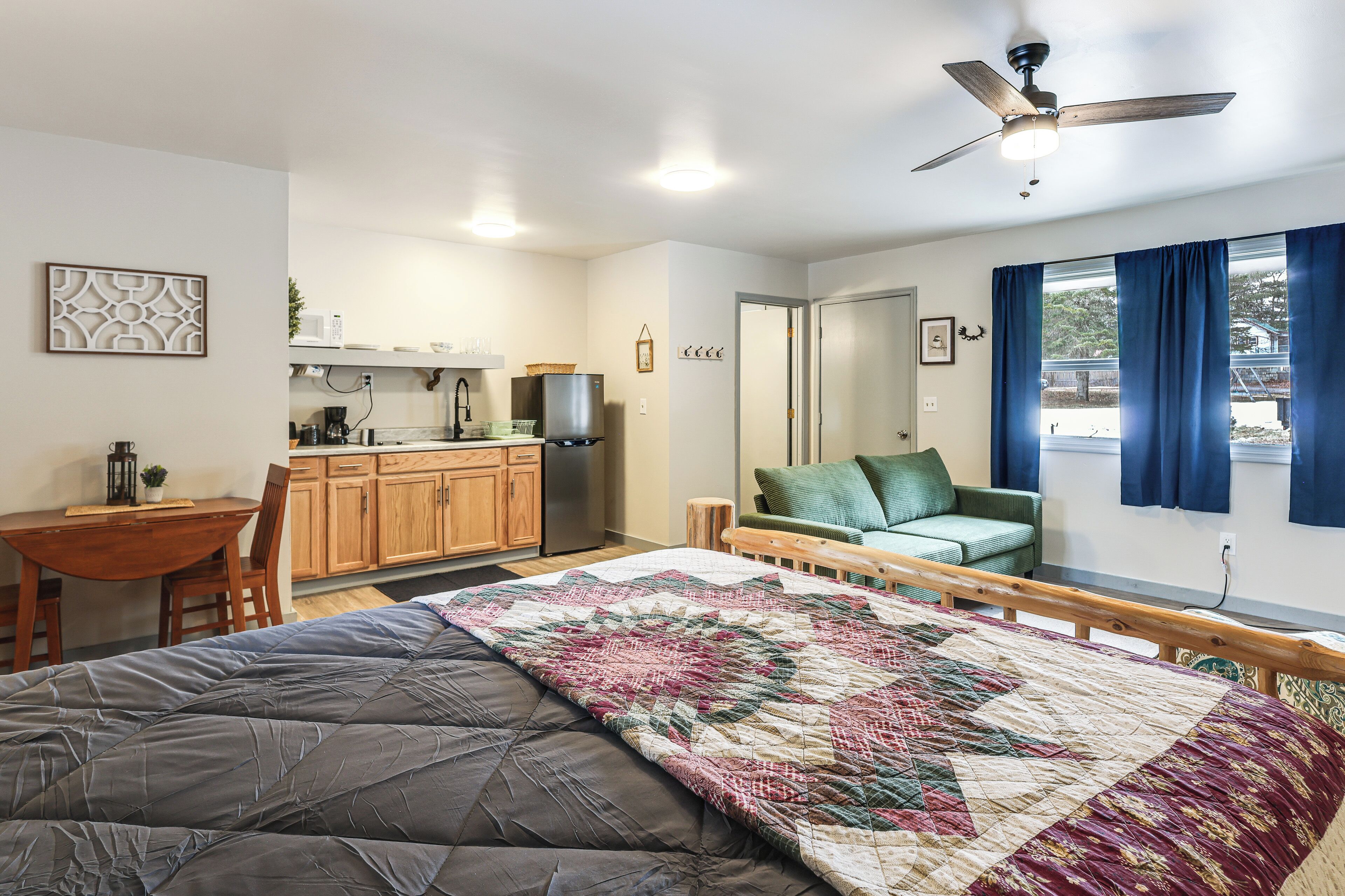 A bedroom with a bed, a desk, a kitchenette, and a view of the outdoors.
