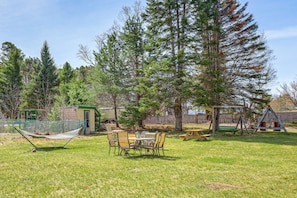 A backyard with a hammock, picnic table, and swing set.
