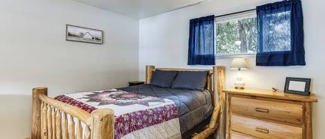 A wooden bed with a quilt, a bedside table with a lamp, and a window with curtains.