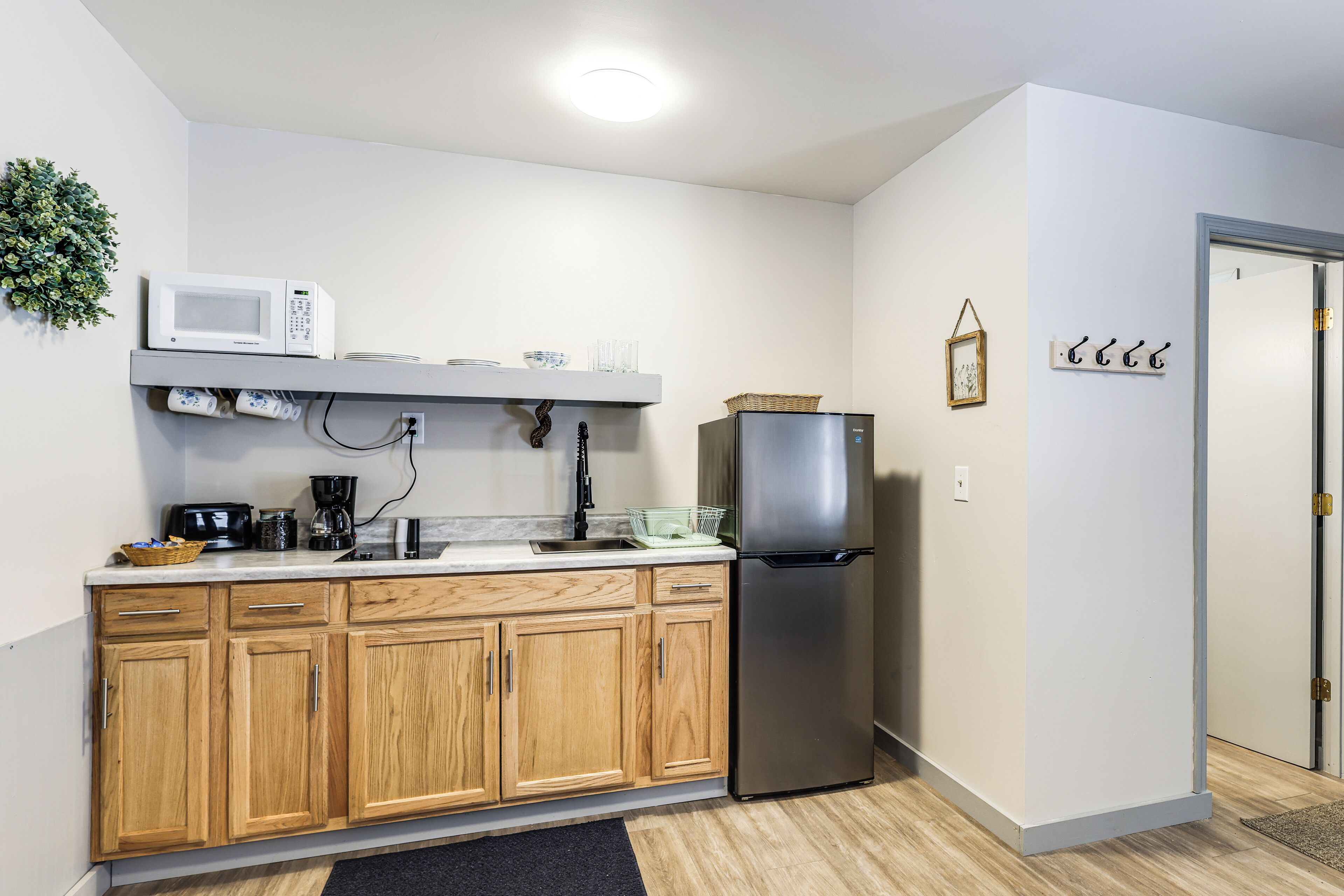 Una cocina compacta con armarios de madera, un refrigerador de acero inoxidable, un microondas y una cafetera.