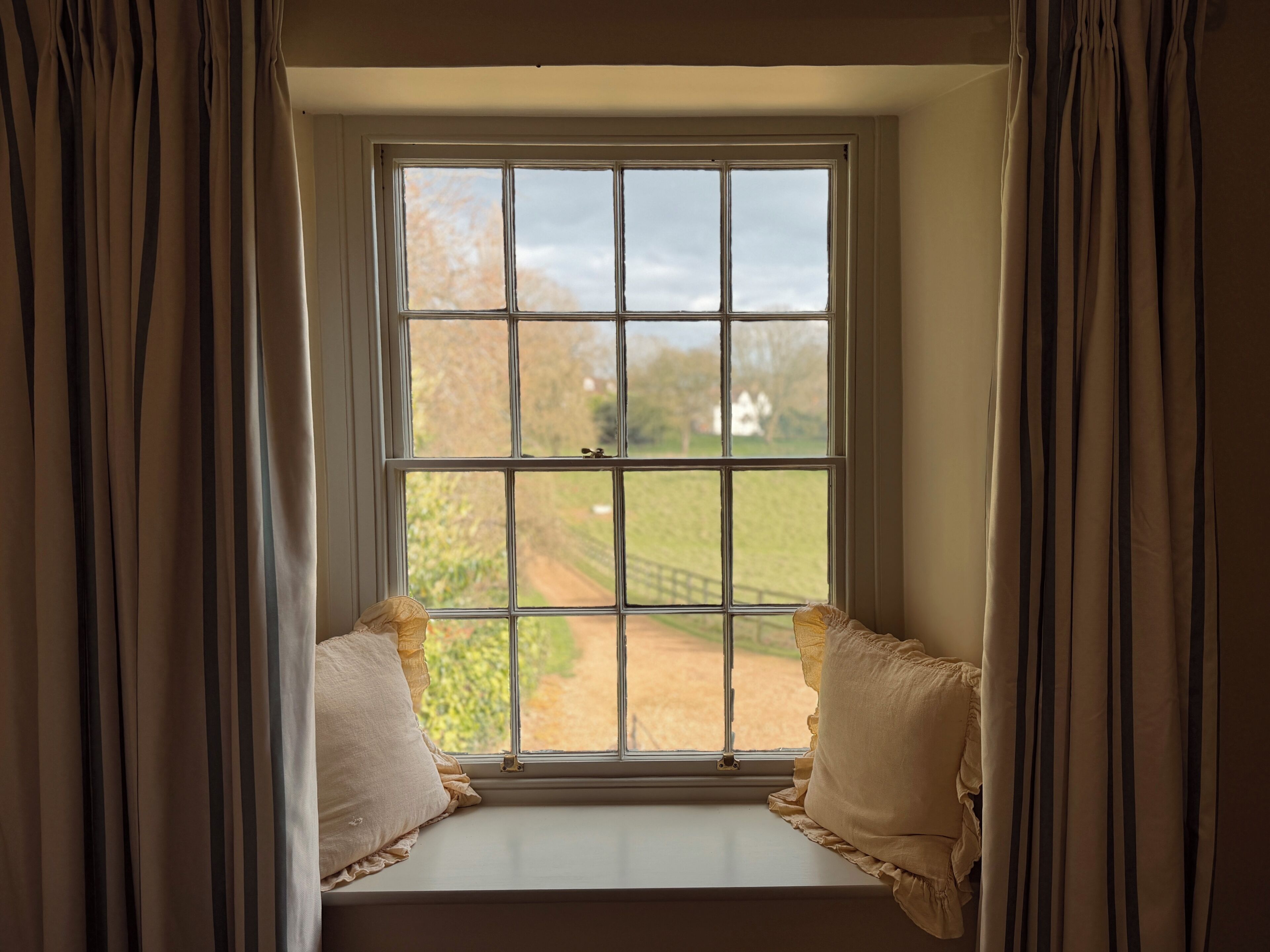 A window with a view of a rural landscape, curtains, and a cushion.