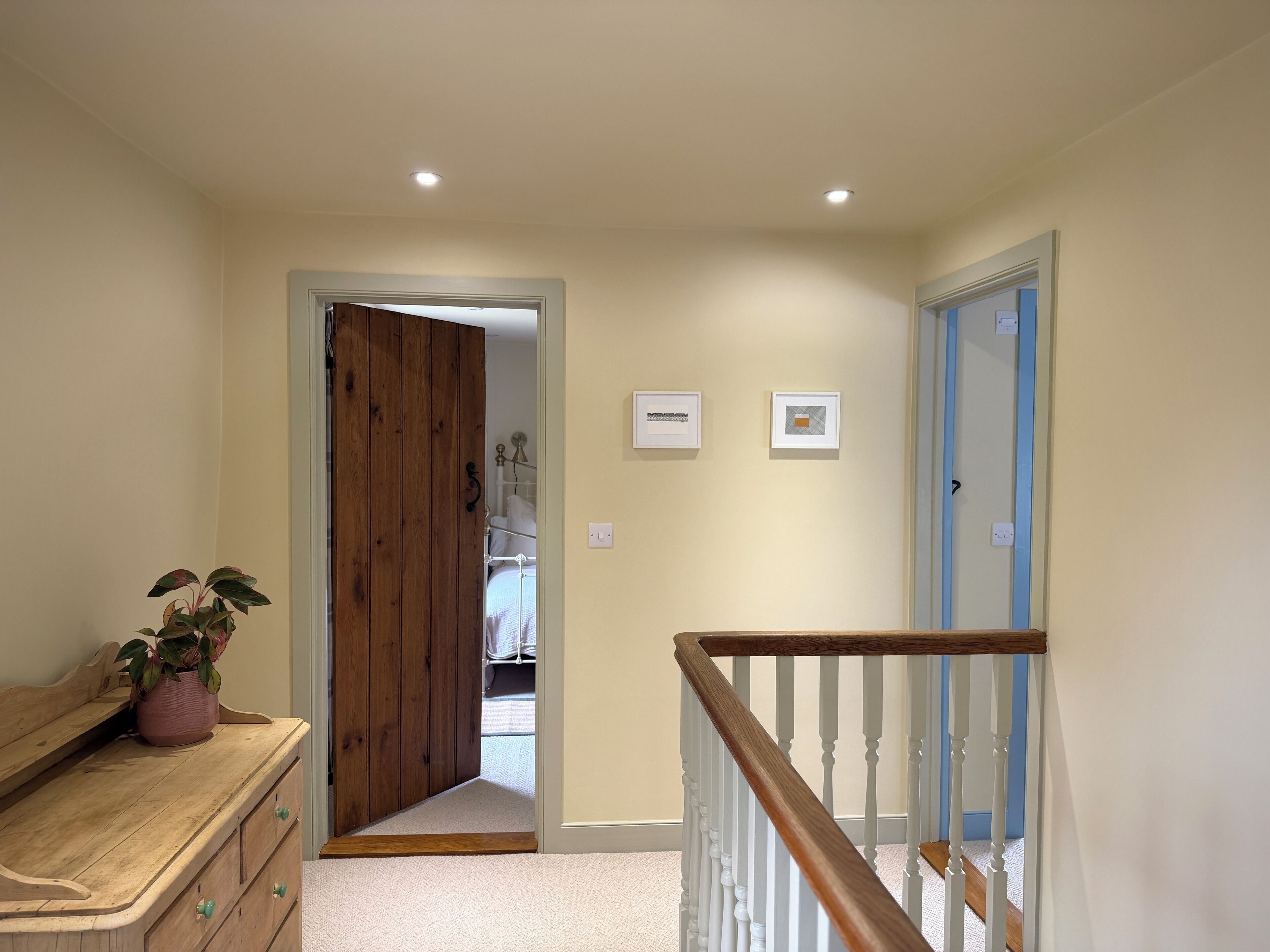 A hallway with a wooden door, a staircase with white balusters, and a potted plant on a dresser.