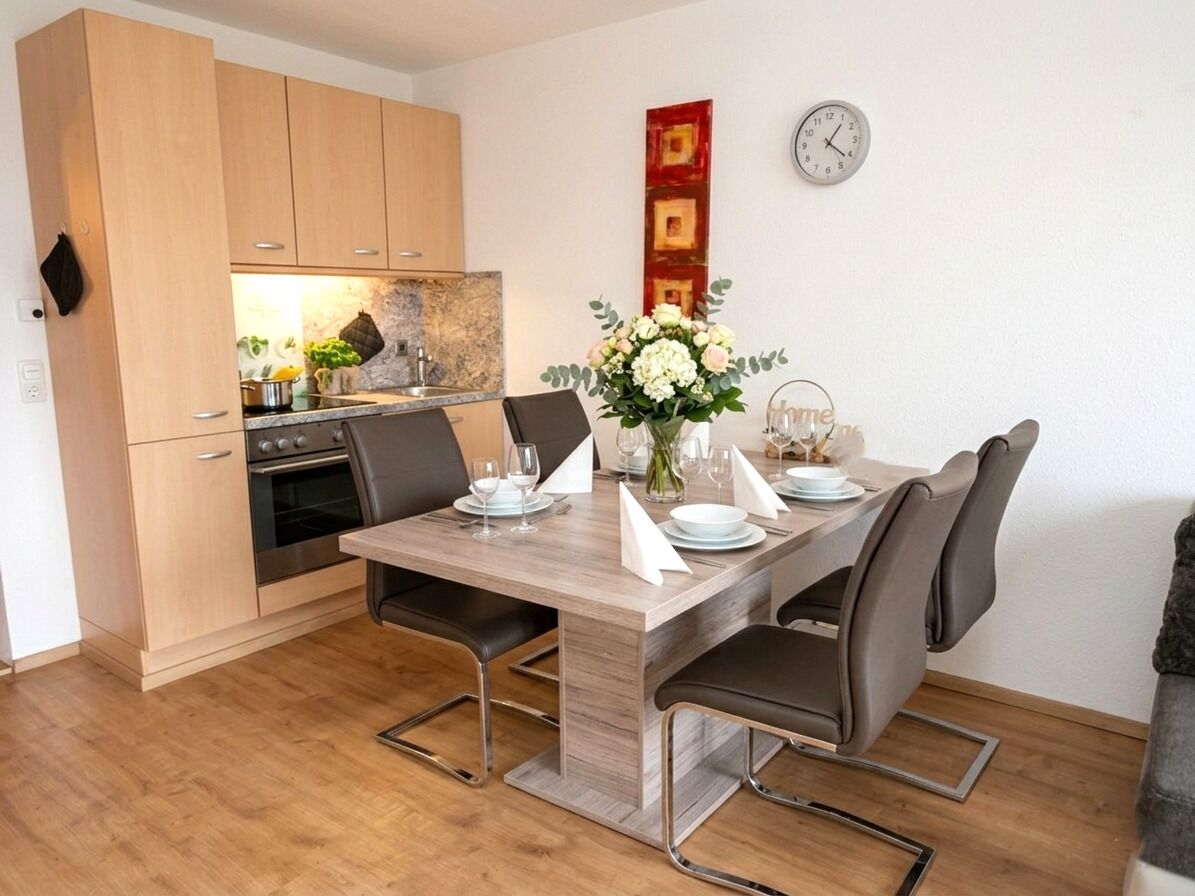 Une cuisine moderne avec des meubles en bois, un four encastré et un coin repas comprenant une table et des chaises en bois.