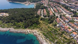 Vista aérea de uma vila costeira com edifícios residenciais, um litoral rochoso e mar azul cristalino.