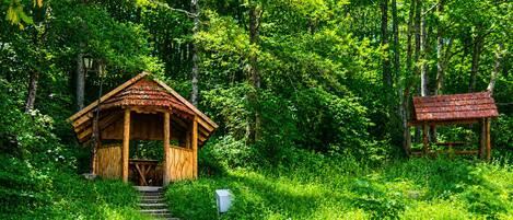 A wooden cabin with a porch and a staircase leading up to it, surrounded by lush greenery.