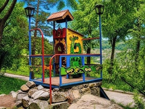 A colorful play structure with a roof, surrounded by trees and rocks.