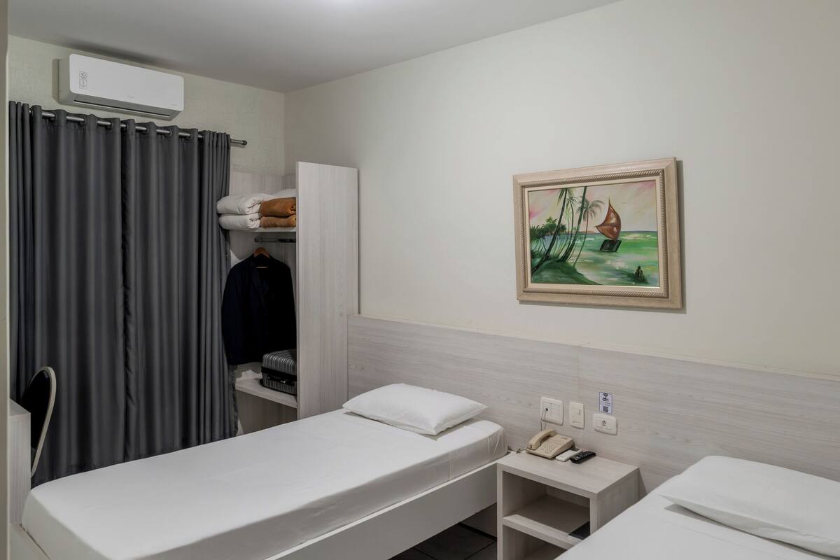 A hotel room with two beds, a wardrobe, a painting, and a telephone on a nightstand.