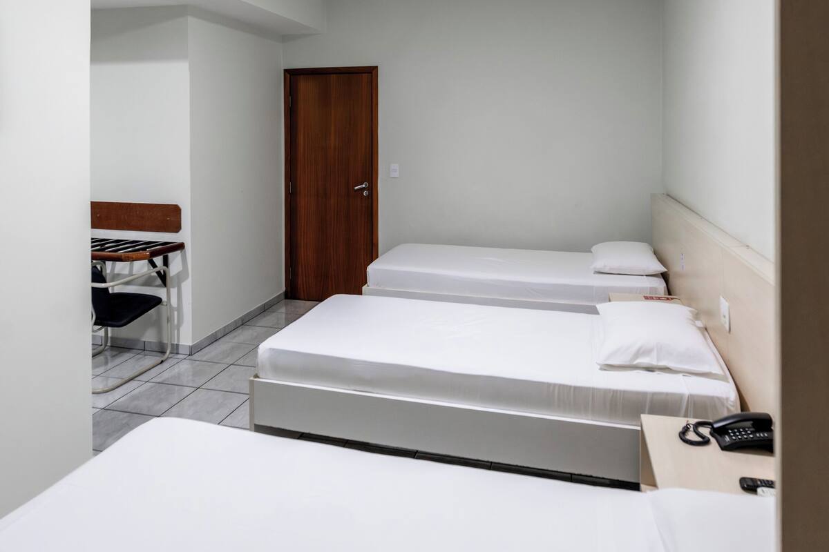 A hotel room with two beds, a desk, a chair, and a door.