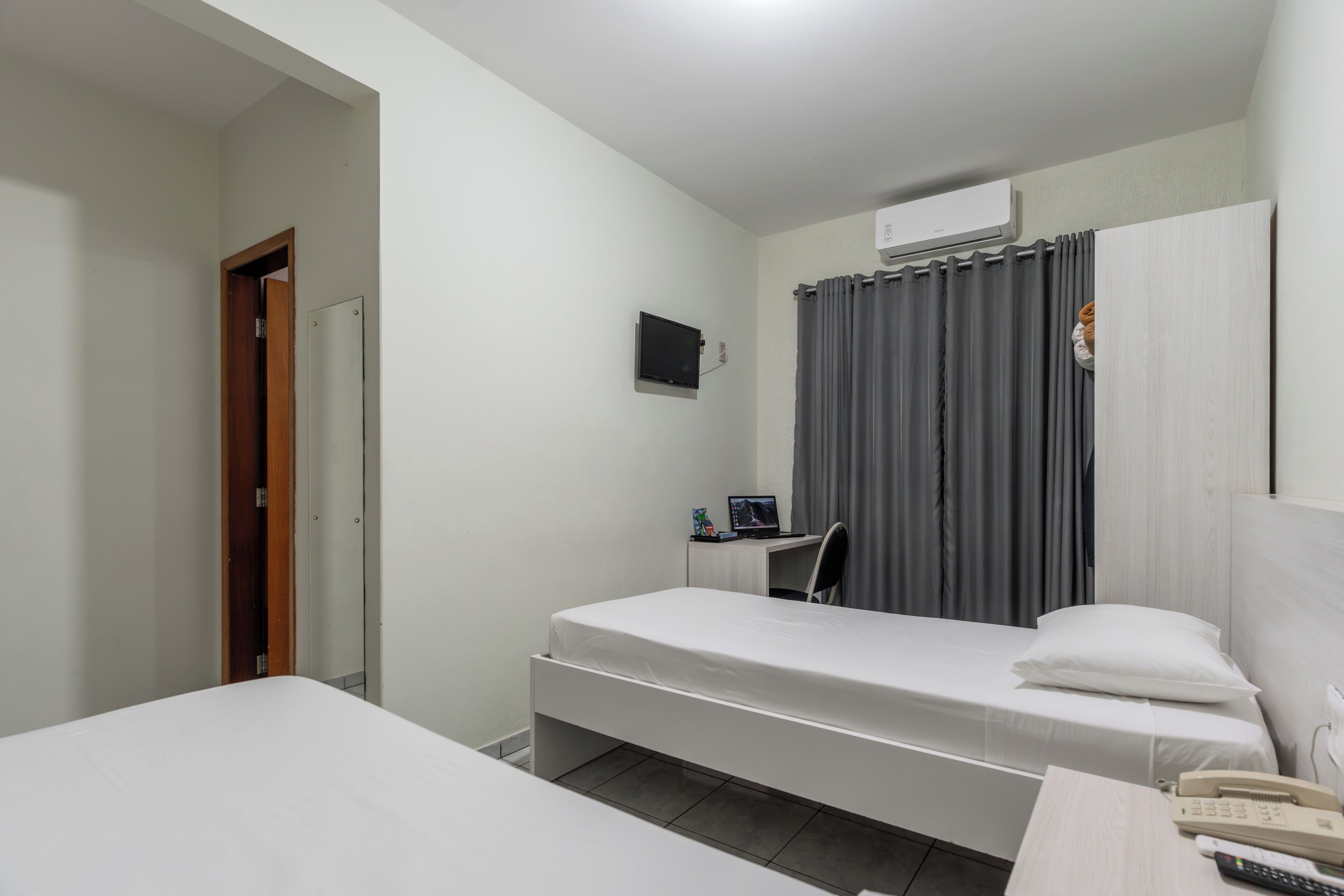 Un dormitorio con dos camas individuales, un escritorio con computadora, teléfono y televisor montado en la pared.
