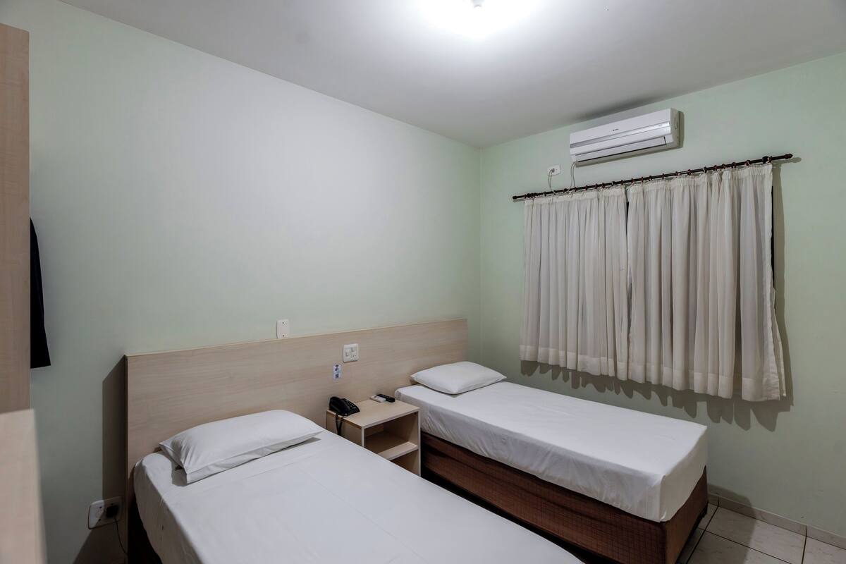 A hotel room with two beds, a bedside table with a phone, an air conditioner, and a curtain.
