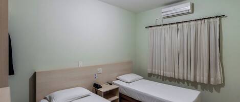 Habitación de hotel con dos camas, una mesita de noche con teléfono, aire acondicionado y una cortina.