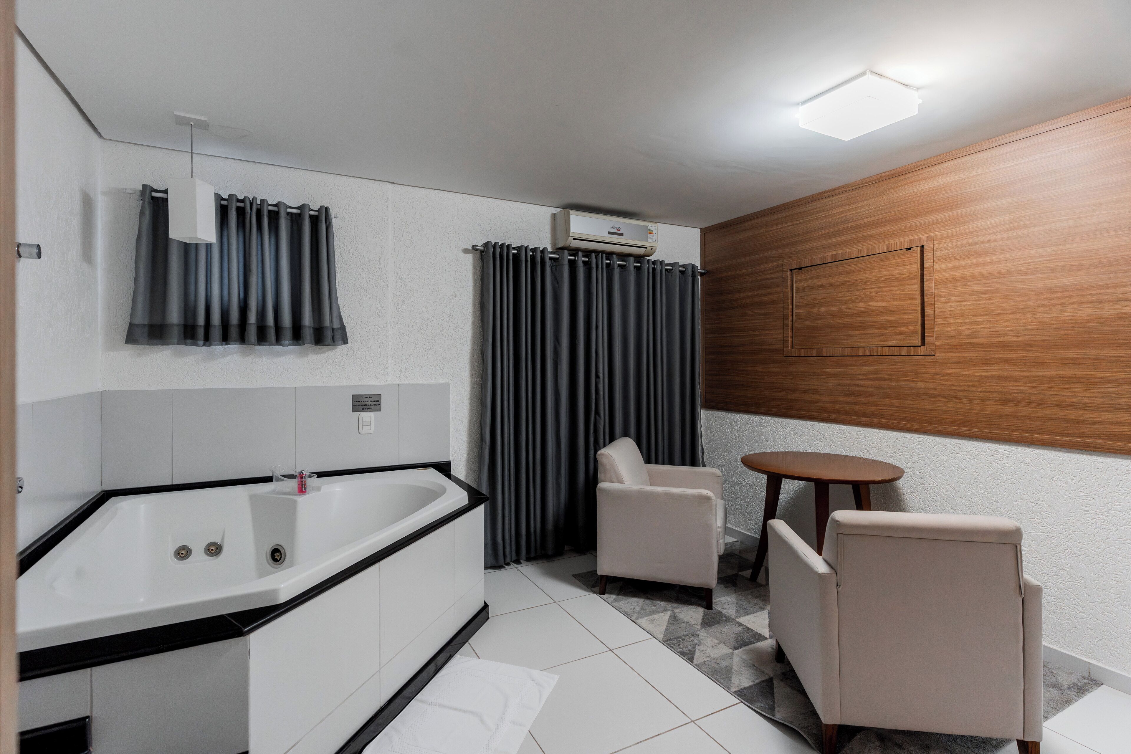 A modern bathroom with a bathtub, a toilet, and a shower. There is a small round table and two chairs.