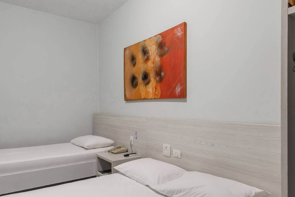 A single-bed room with a wooden headboard, a bedside table with a lamp, and a wall-mounted painting.