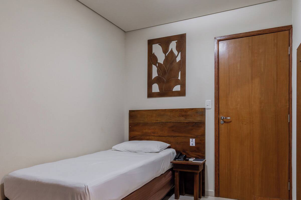 A single bed with a wooden headboard, a bedside table, a wooden wardrobe, and a wall-mounted artwork.