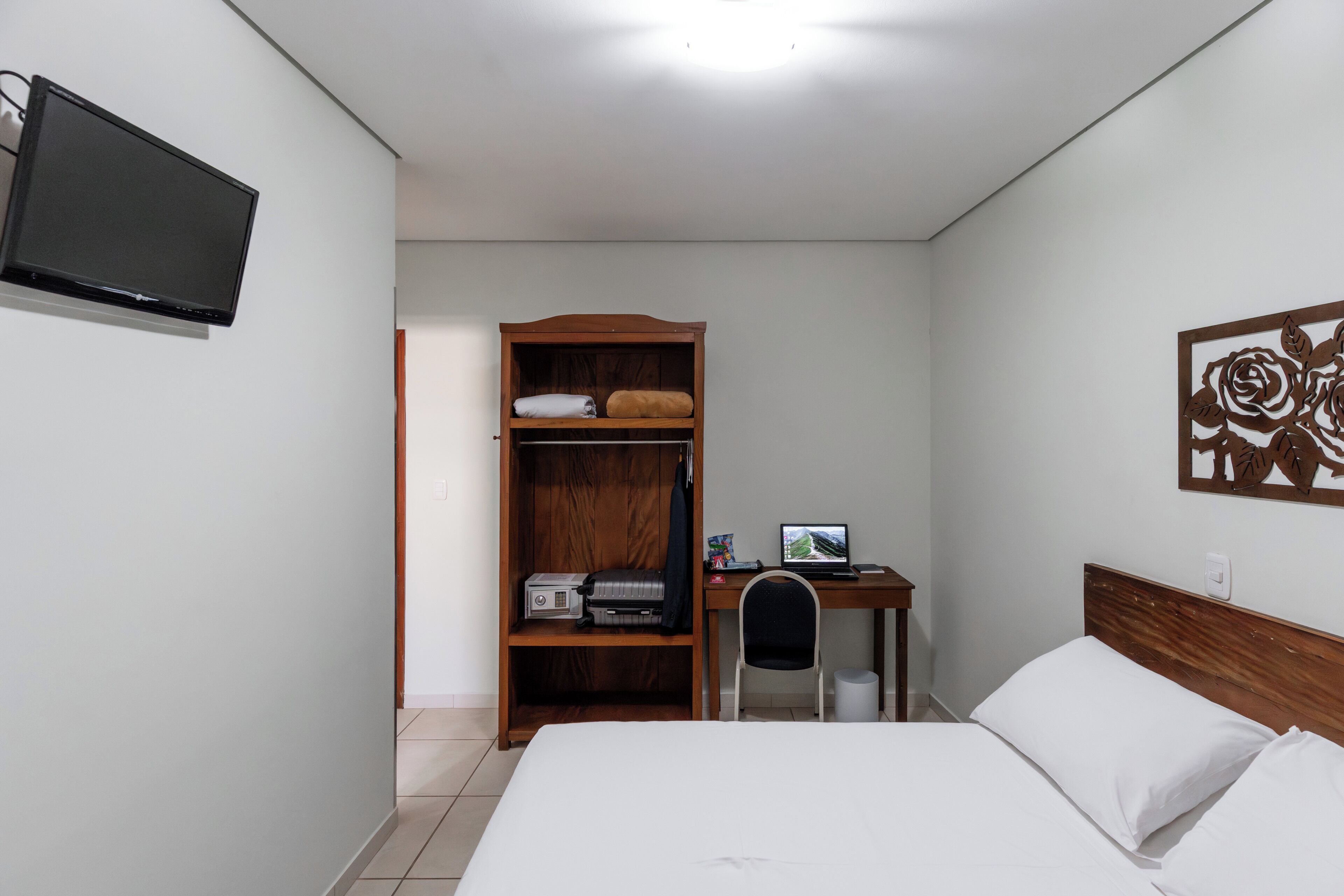A hotel room with a bed, a desk with a computer, a wardrobe, and a TV mounted on the wall.