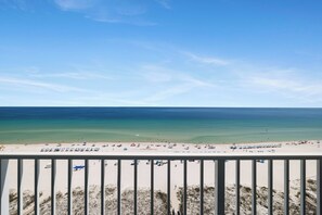 A beach view with a railing, clear sky, and calm sea. - Lighthouse 1009 by Liquid Life (Gulf Shores)