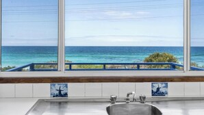Una cocina con un ventanal grande que da al océano, un lavamanos y un salpicadero de azulejos con una cruz.