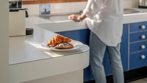 Una persona de pie junto a una encimera de cocina, con vista al mar a través de una ventana.