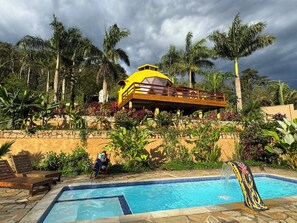 A pool area with a yellow building, palm trees, and a person reading a book.