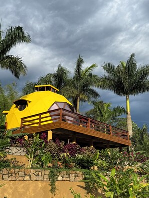 A yellow building with a wooden deck, surrounded by palm trees and tropical plants.