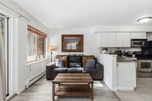 Een moderne woonkamer met een bank, een salontafel en een keuken met apparatuur.