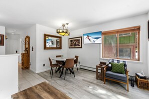 Een eetgedeelte met een ronde tafel, stoelen en een kroonluchter. Er is een bank met uitzicht op het omliggende landschap.