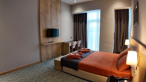 Une chambre d’hôtel avec un lit, un bureau, une télévision et une fenêtre avec des rideaux.