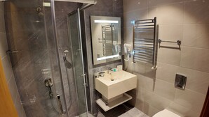 Une salle de bain moderne avec une douche à parois de verre, un lavabo blanc, un miroir et un porte-serviettes.