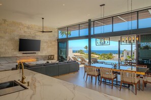 A modern kitchen with a large island, a flat-screen TV, and a stone wall. - Dual Modern Luxe Villas Sleeps 22 w/ Pools, Hot Tubs & Ocean Views Near Marina (Cabo San Lucas)