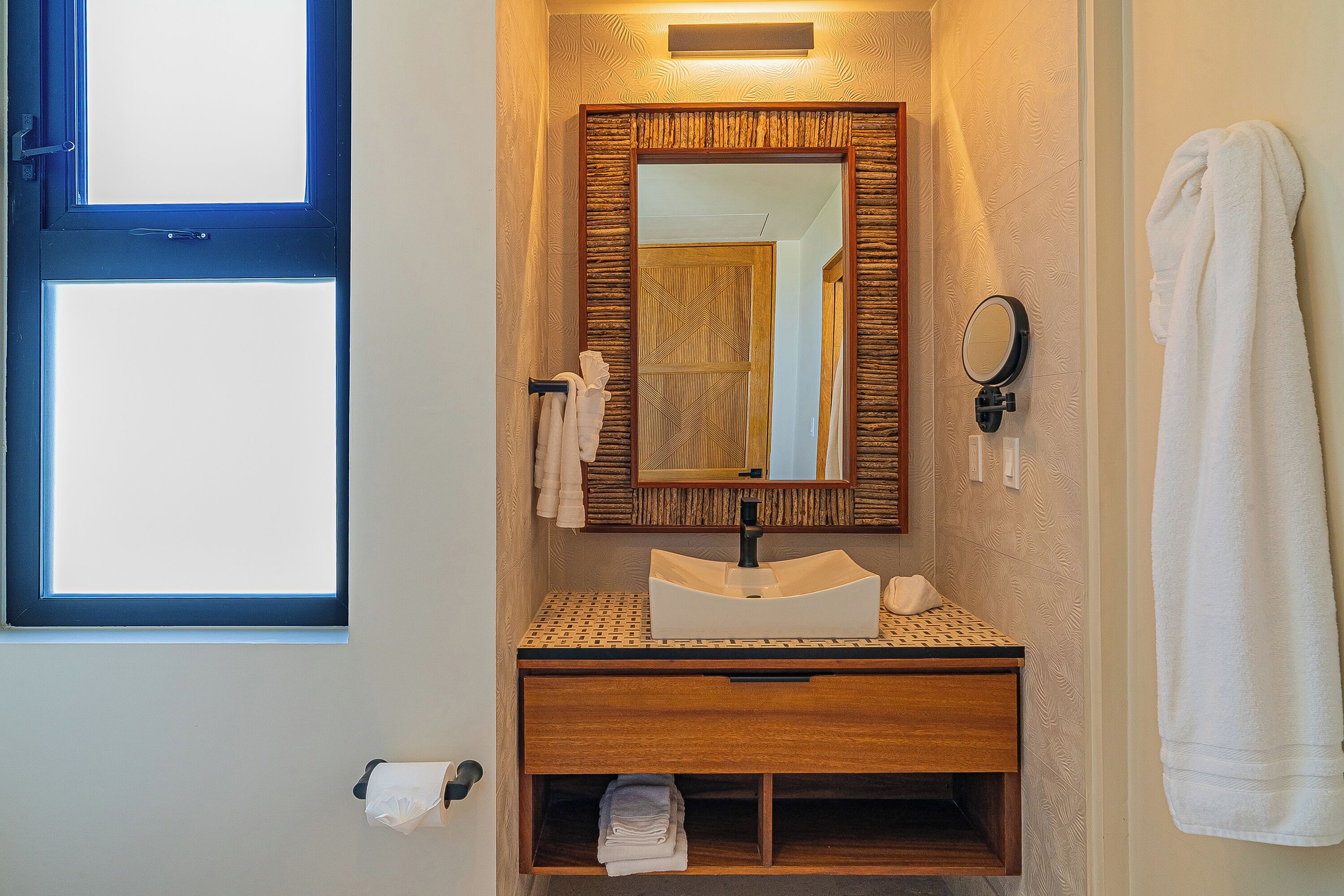 Un baño con tocador de madera, lavabo, espejo y perchero para toallas.