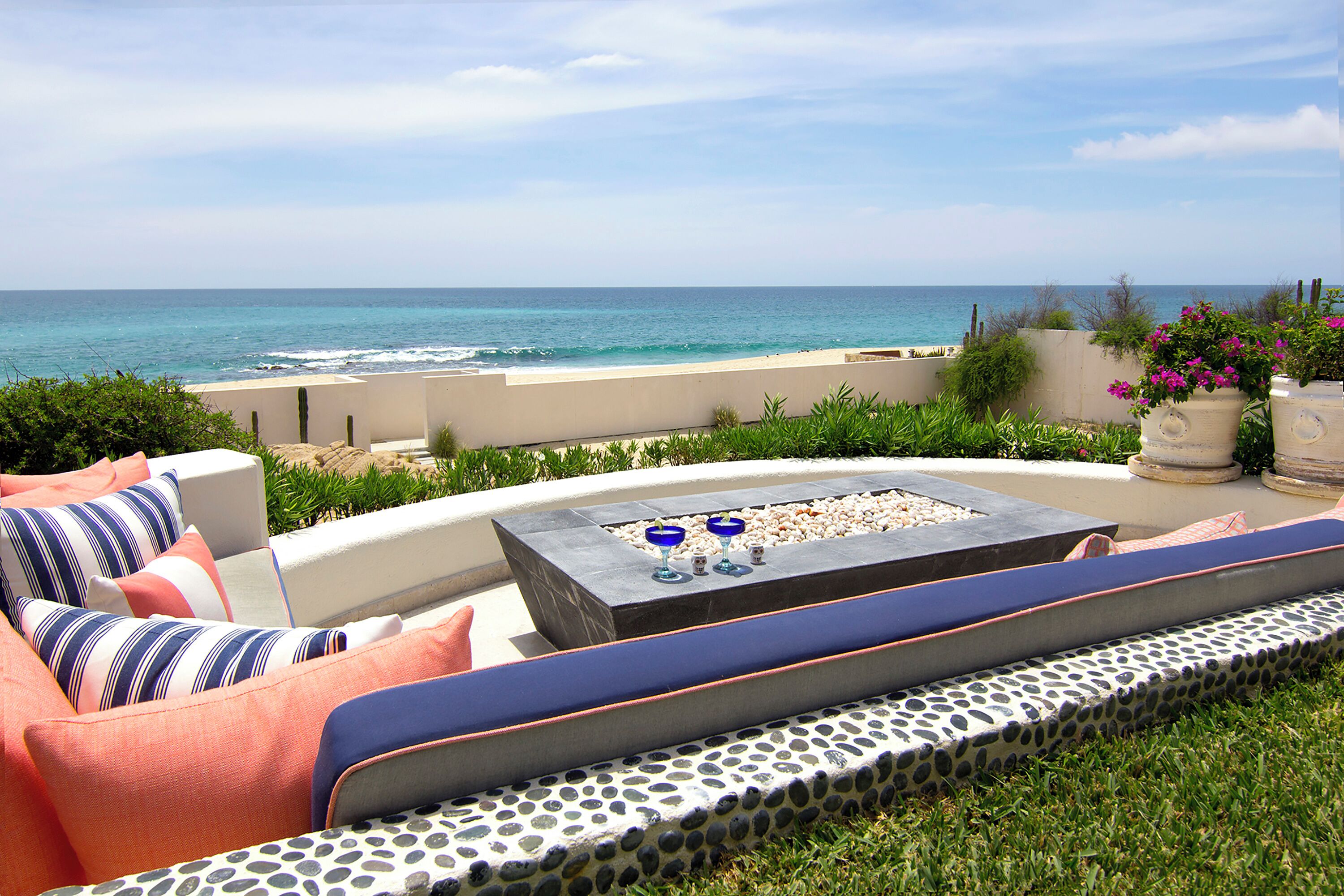 An outdoor seating area with a view of the ocean, a fire pit, and a garden with plants.