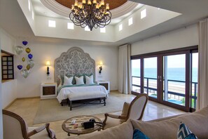 A spacious bedroom with a large bed, a chandelier, a balcony with a view of the beach, and a sitting area with a coffee table. - Beachfront 12BR Compound w/ Pools, Hot Tubs, Game Rooms & Ocean Views Cabo (Cabo San Lucas)