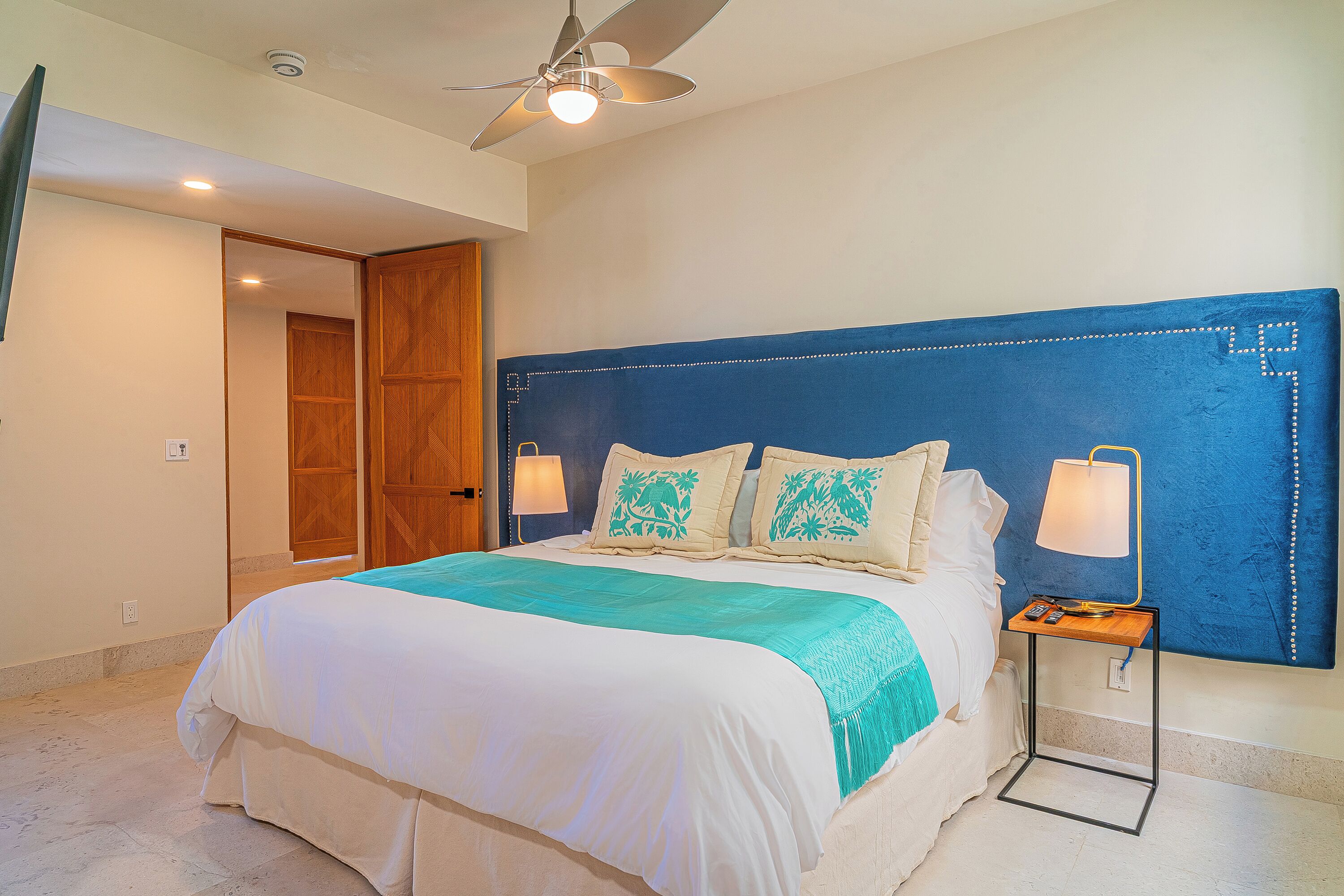 A bedroom with a bed, a ceiling fan, a nightstand, and a wall-mounted lamp.