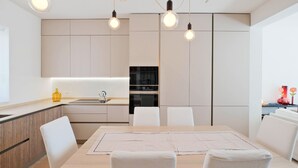 Eine moderne Küche mit Essbereich, ausgestattet mit einem Holztisch, weißen Stühlen und Pendelleuchten.