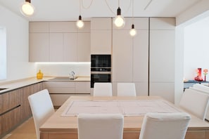Eine moderne Küche mit Essbereich, ausgestattet mit einem Holztisch, weißen Stühlen und Pendelleuchten.