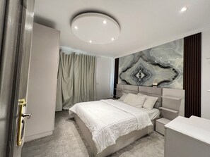 A modern bedroom with a bed, bedside tables, a headboard, and a ceiling light fixture. - ELITE Premium 3 En-Suites Nile Residence (Giza)