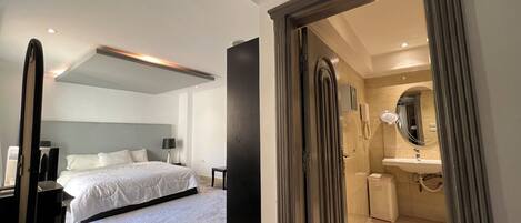 A modern hotel room with a large bed, a separate bathroom with a mirror and sink, and a walk-in closet.