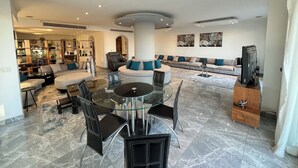 Een ruime woonkamer met een ronde glazen tafel, zwarte stoelen, een bank en een televisie.