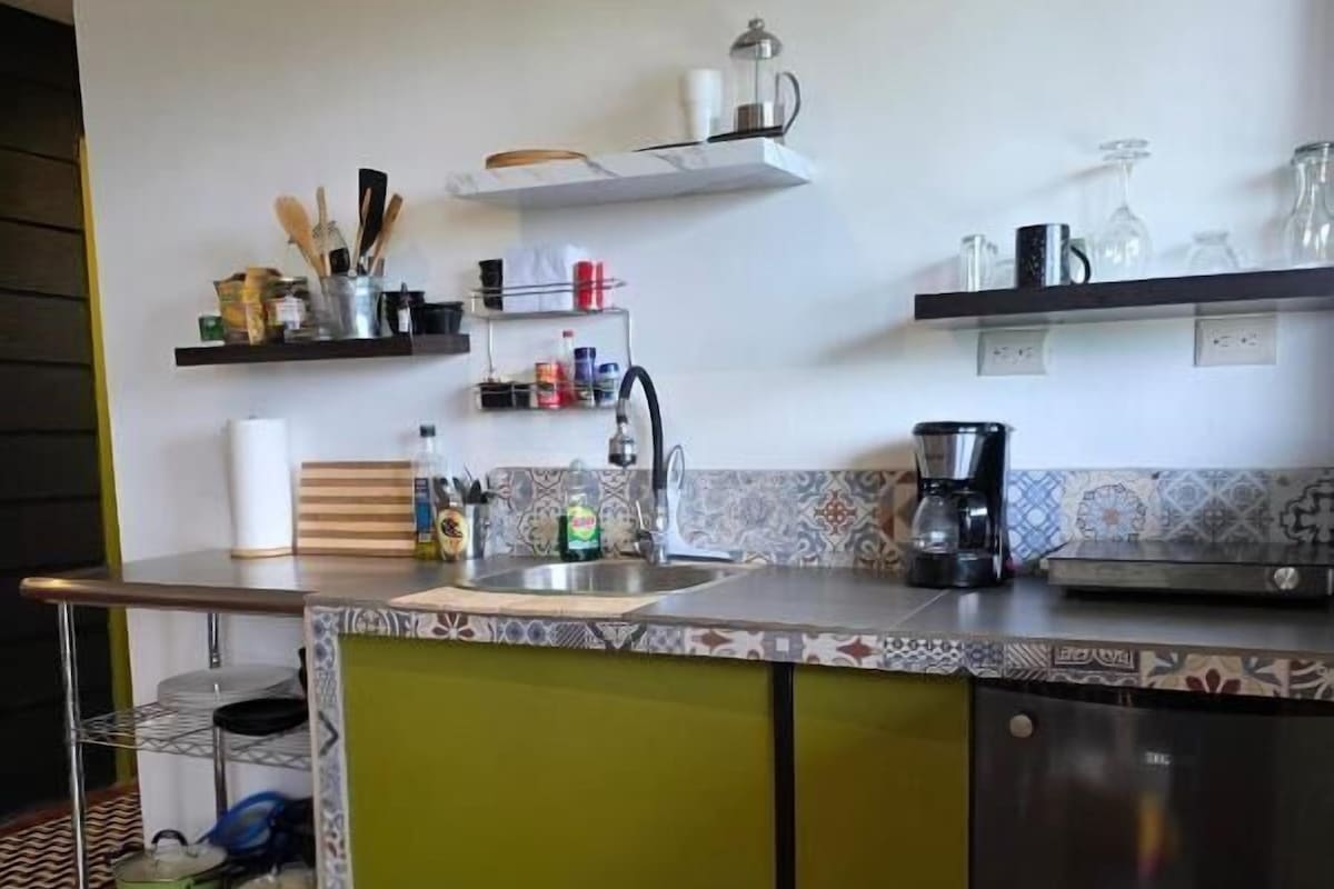 A kitchen with a green island, stainless steel appliances, and shelves with kitchen items.