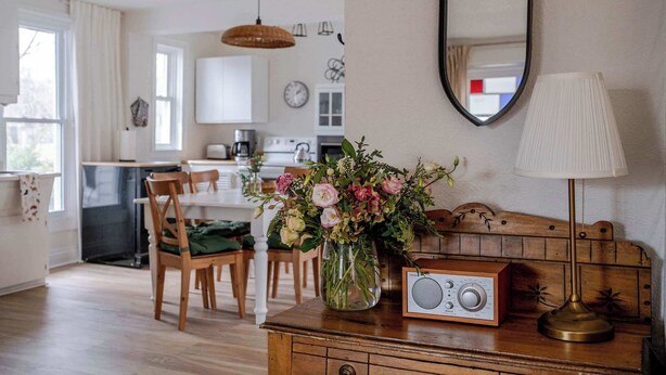 Ein Essbereich mit Holztisch, Stühlen, einem Blumenstrauß, einem Radio und einer Lampe.