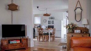Ein Wohnzimmer mit Fernseher, Holzmöbeln, einem Essbereich mit Stühlen und einer Küche im Hintergrund.