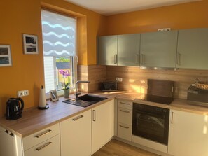A modern kitchen with a sink, stove, and microwave. There are cabinets and a window with blinds. - Thaleblick Apartment with a rooftop terrace & mountain views   (Thale)
